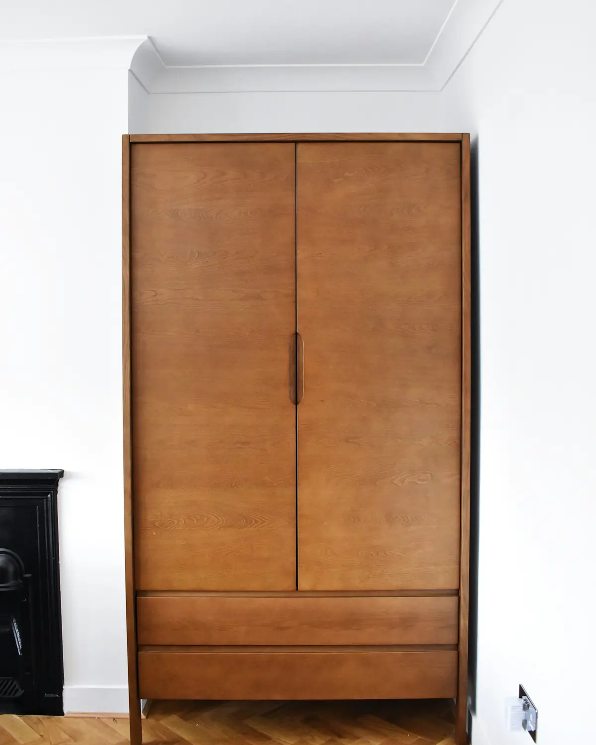 Armoire à deux portes en chêne huilé aux lignes simples, contre un mur blanc