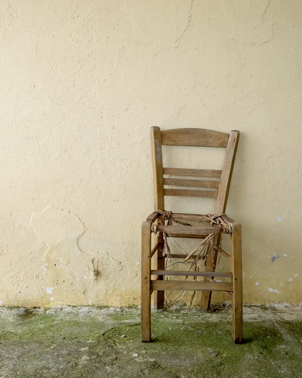Chaise paillée ancienne à la paille défaite, posée contre un mur décrépi