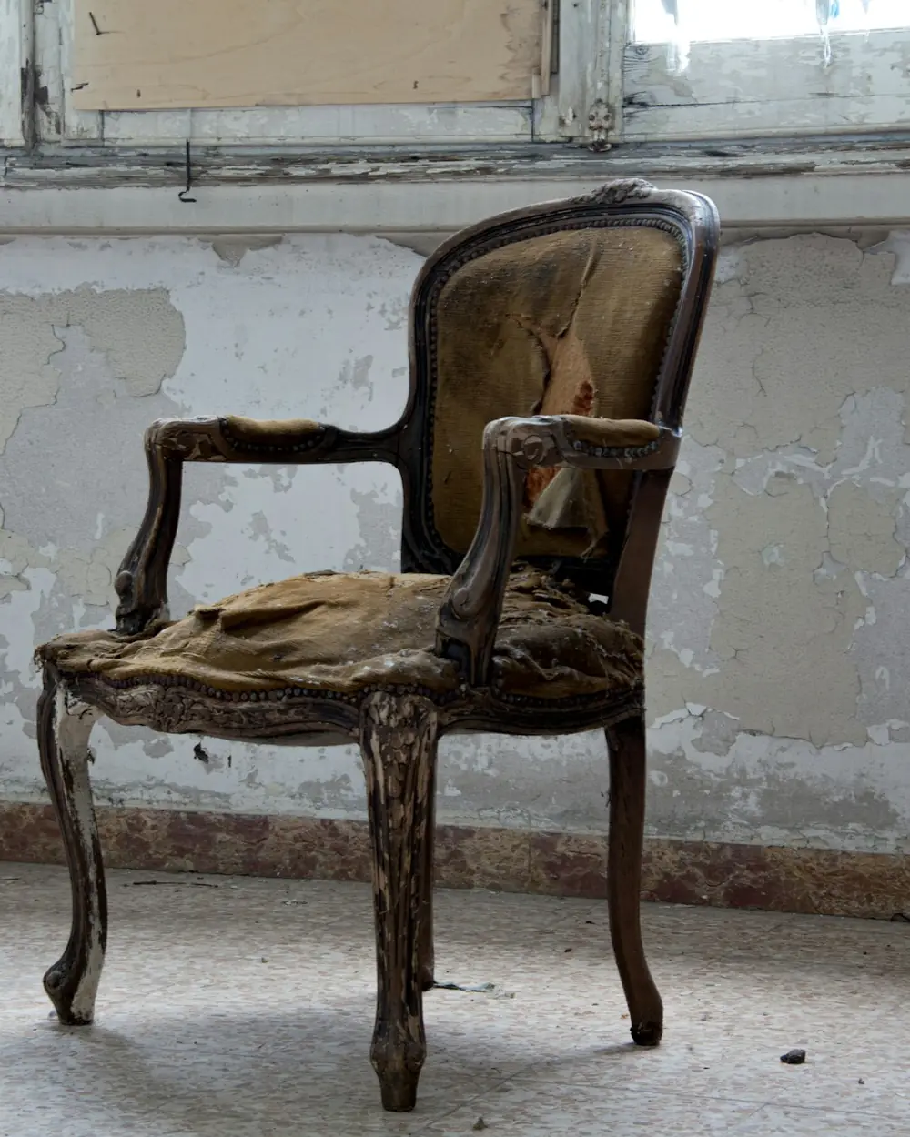 Fauteuil ancien de style Louis XV au tissu déchiré, dans une pièce abandonnée