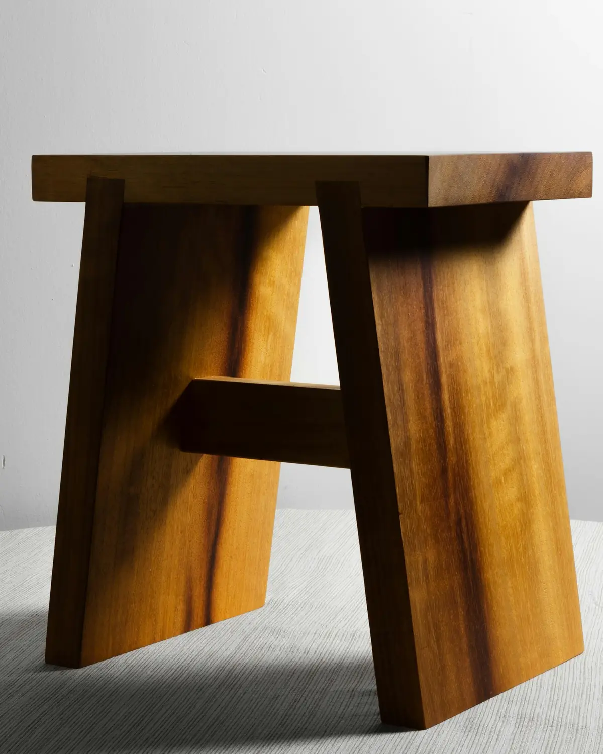Tabouret massif en noyer aux pieds évasés, sur fond clair